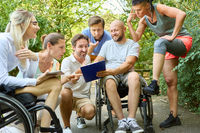 Inclusive group of friends sharing a laugh in a park, with individuals using a wheelchair and prosthetic leg