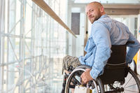 Smiling man in wheelchair enjoying sunshine in modern building