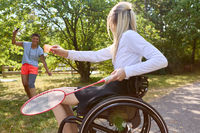 Woman in wheelchair playing badminton with friend in sunny park