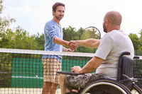 Inclusive sportsmanship: Man in wheelchair shaking hands over tennis net with standing player