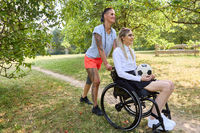 Woman in wheelchair enjoying a sunny day in the park with a friend holding a soccer ball