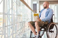 Man in wheelchair holding a shopping bag inside a modern building, showcasing independence